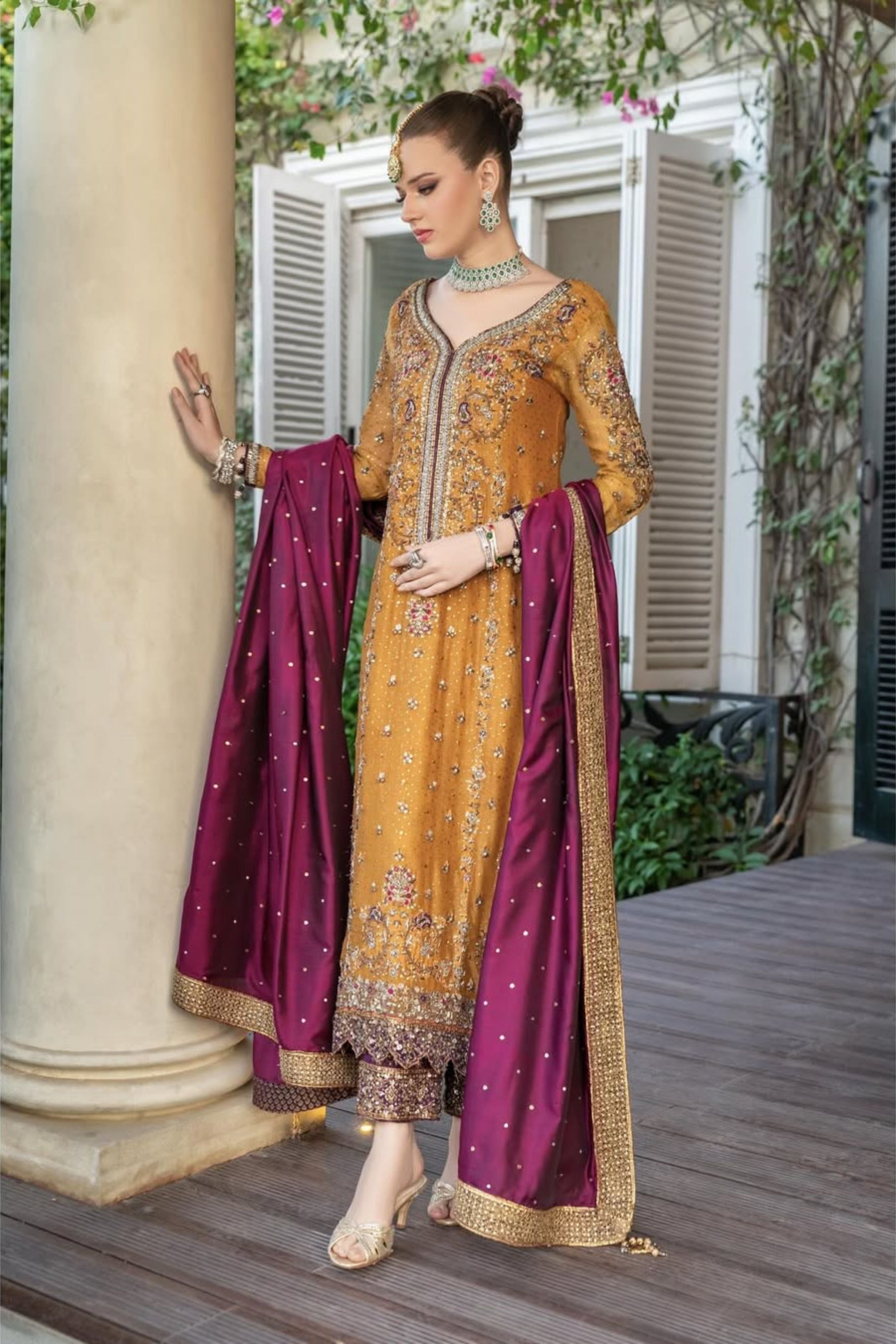 Woman in a traditional yellow and purple outfit standing outdoors.