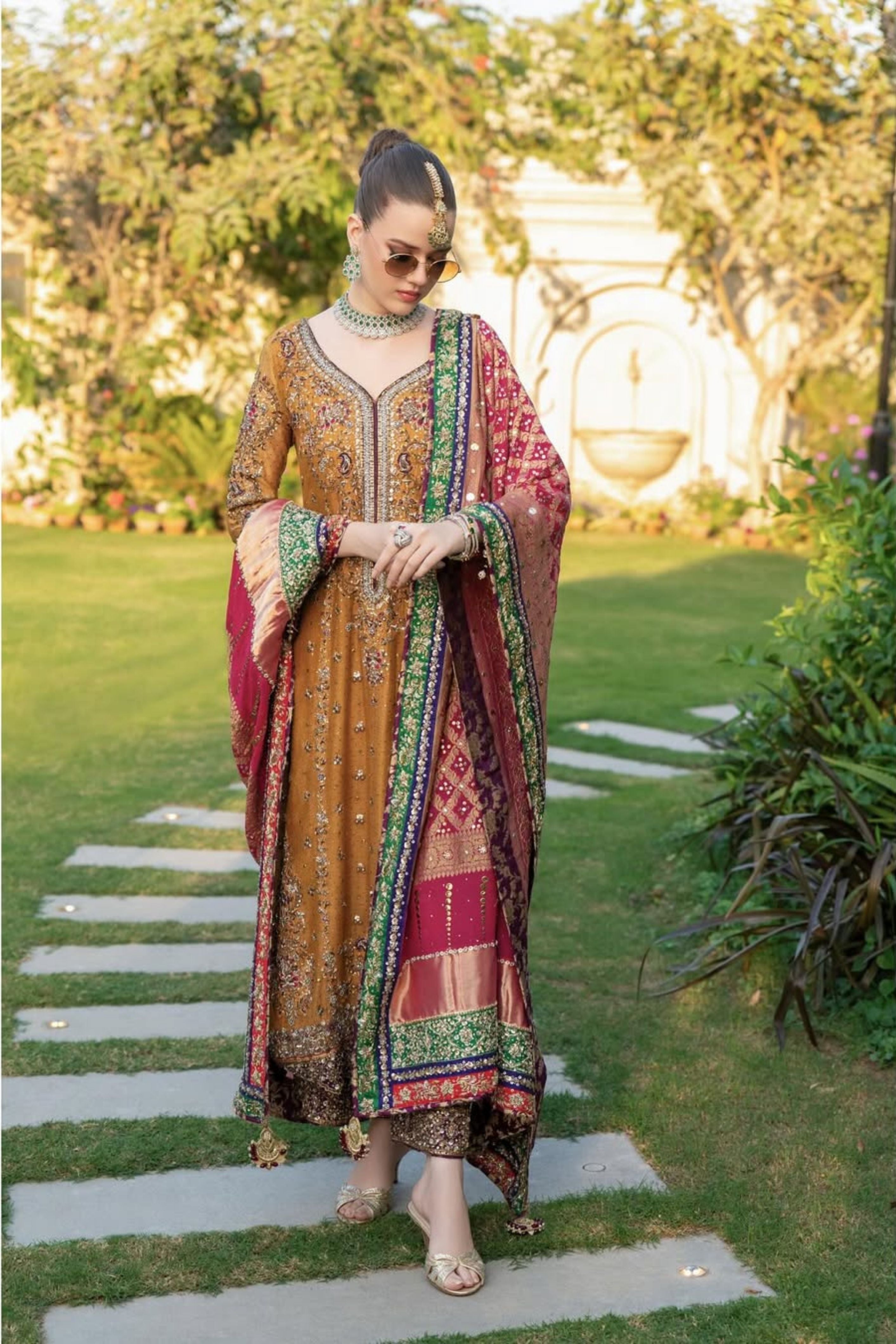 Woman in traditional outfit standing on a stone path with greenery in the background