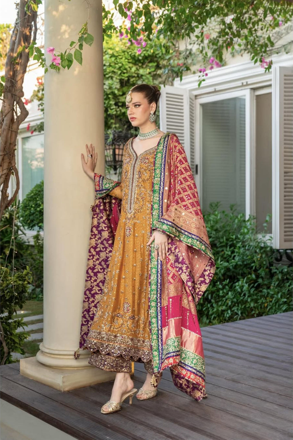 Woman in traditional outfit standing on a wooden deck with greenery in the background