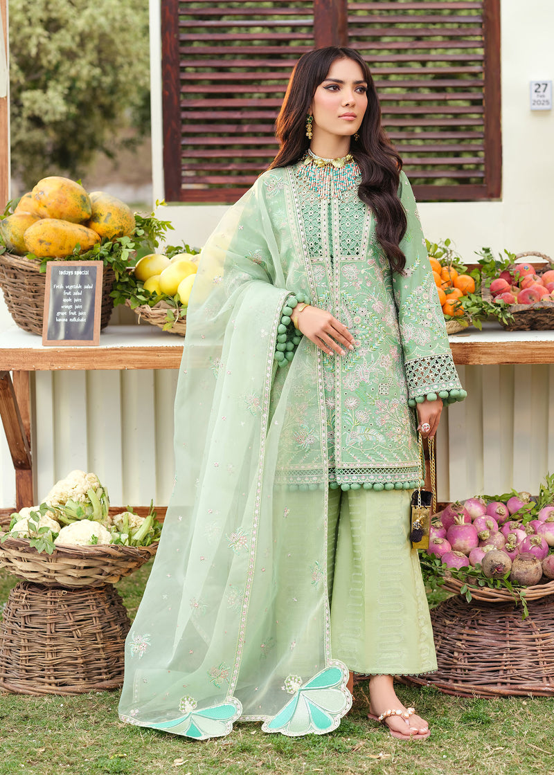 Woman in a light green traditional outfit standing in front of a market stall with fruits and vegetables.