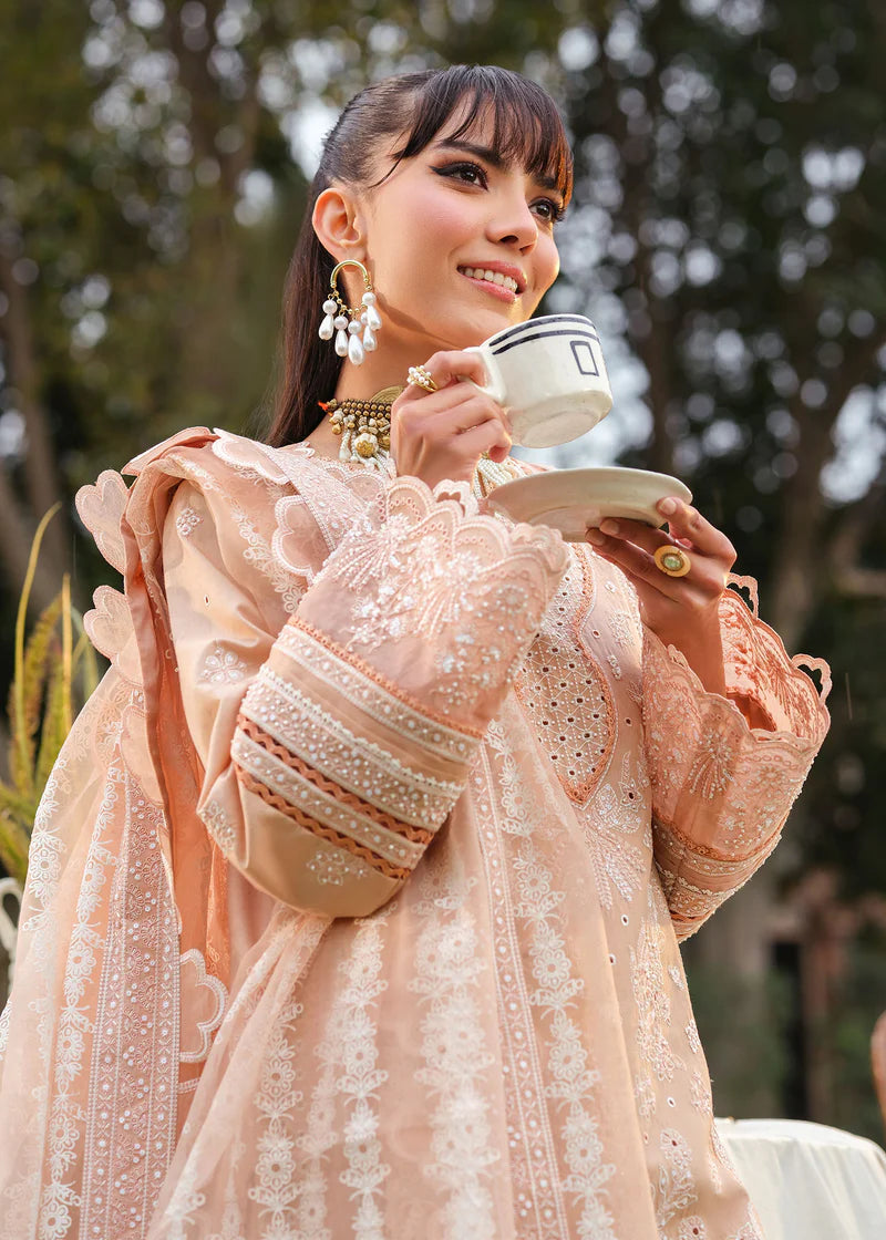 Woman in a peach embroidered outfit holding a teacup outdoors.