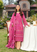 Woman in a pink traditional outfit standing outdoors near a table with a garden and building in the background.