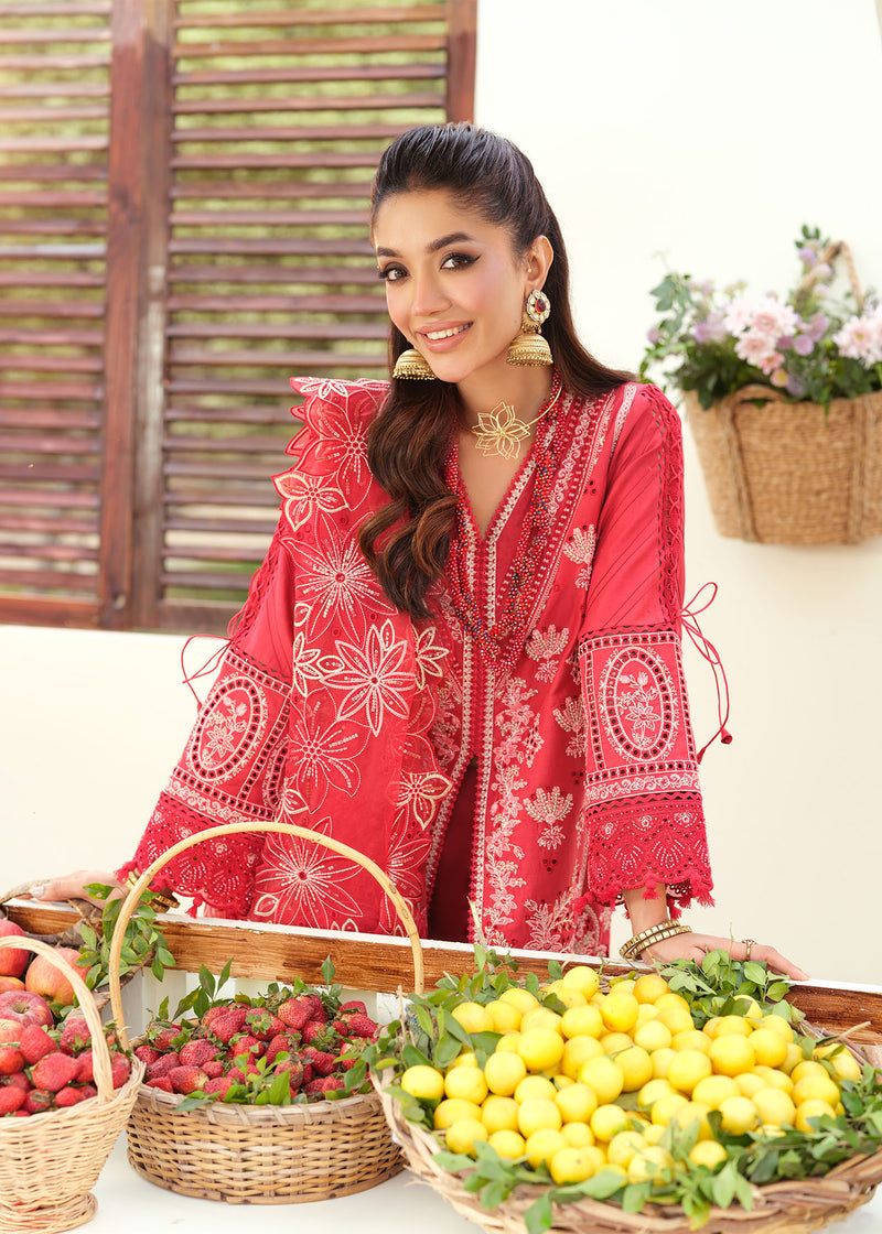 Woman in a red embroidered outfit standing behind baskets of fruits and vegetables.