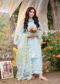 Woman in a light blue embroidered dress holding flowers in an outdoor setting with art and plants.