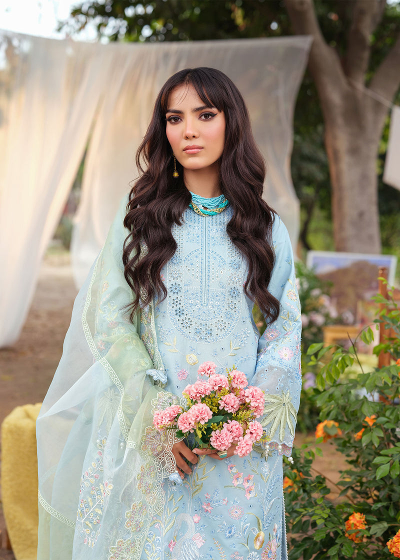 Woman in a light blue embroidered outfit holding pink flowers outdoors.