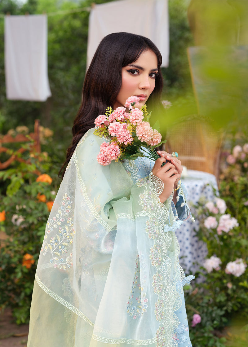 Woman in a light blue traditional outfit holding pink flowers in a garden setting