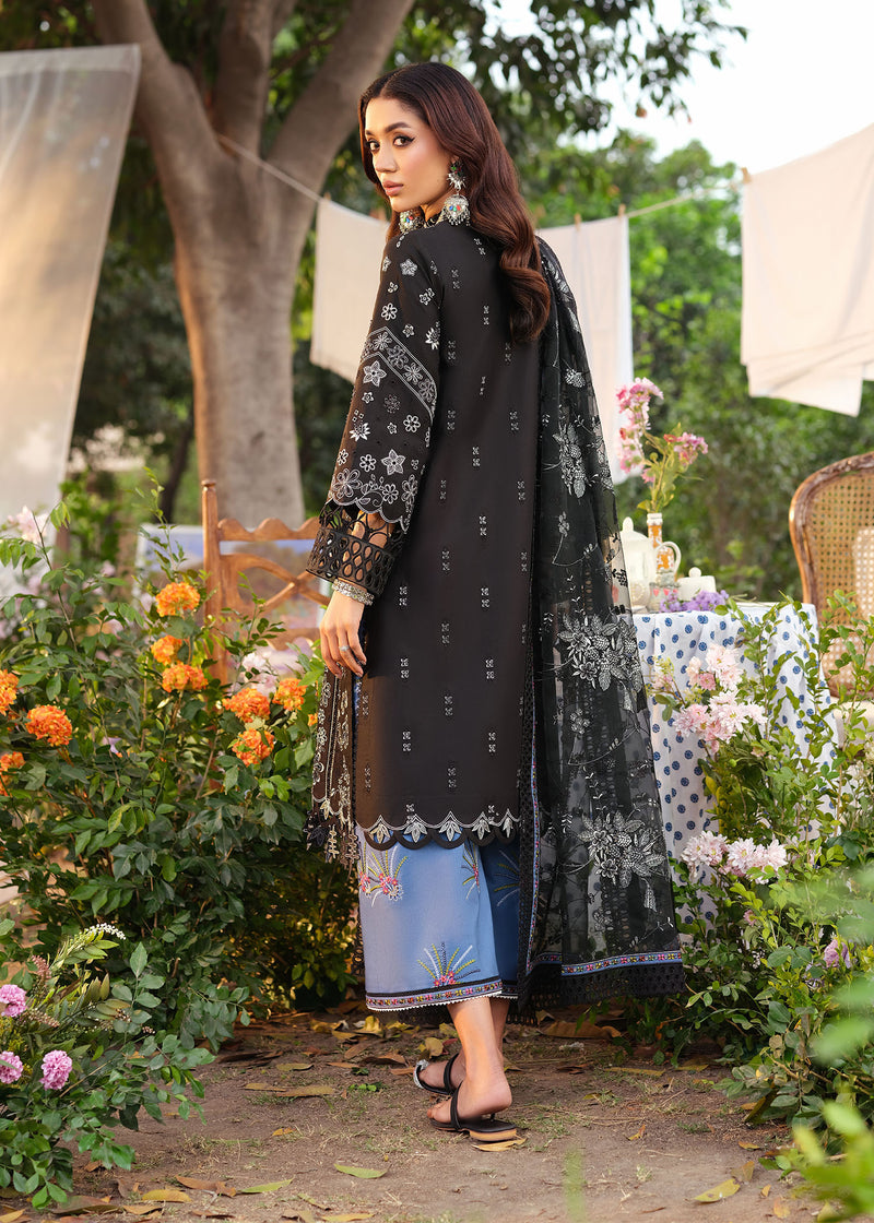 Woman in a black embroidered outfit standing in a garden setting with flowers and tables.