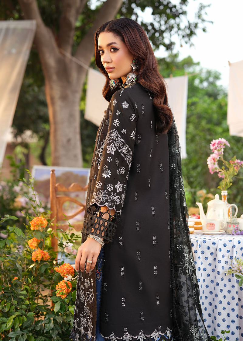 Woman in black embroidered outfit standing outdoors with floral decorations and a table in the background