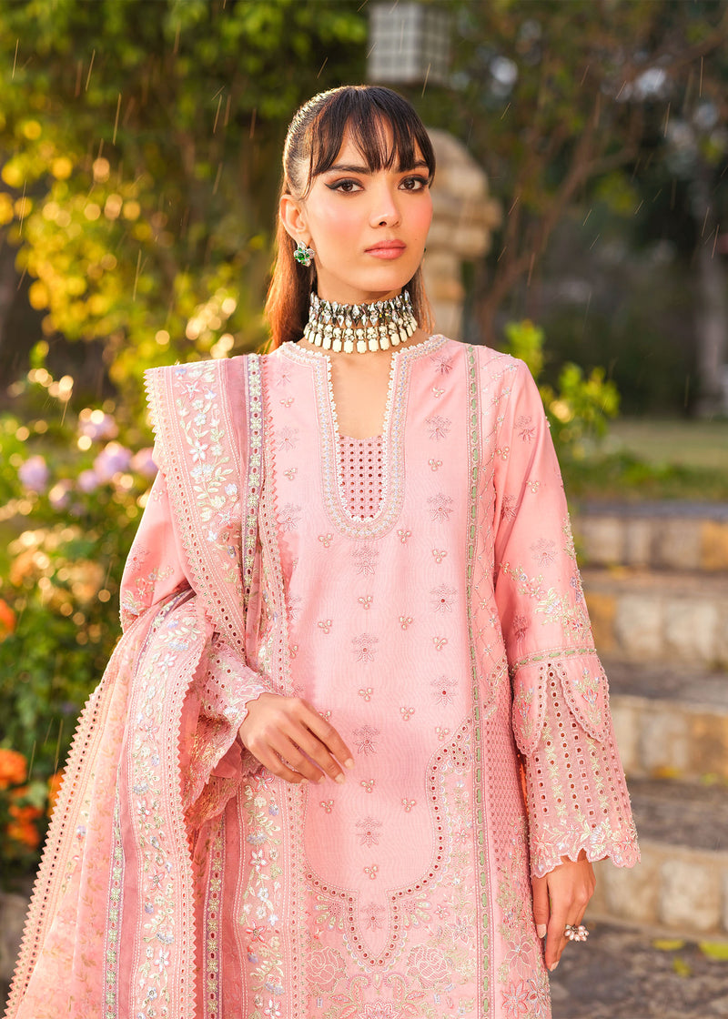 Woman in a pink embroidered outfit standing outdoors with greenery in the background
