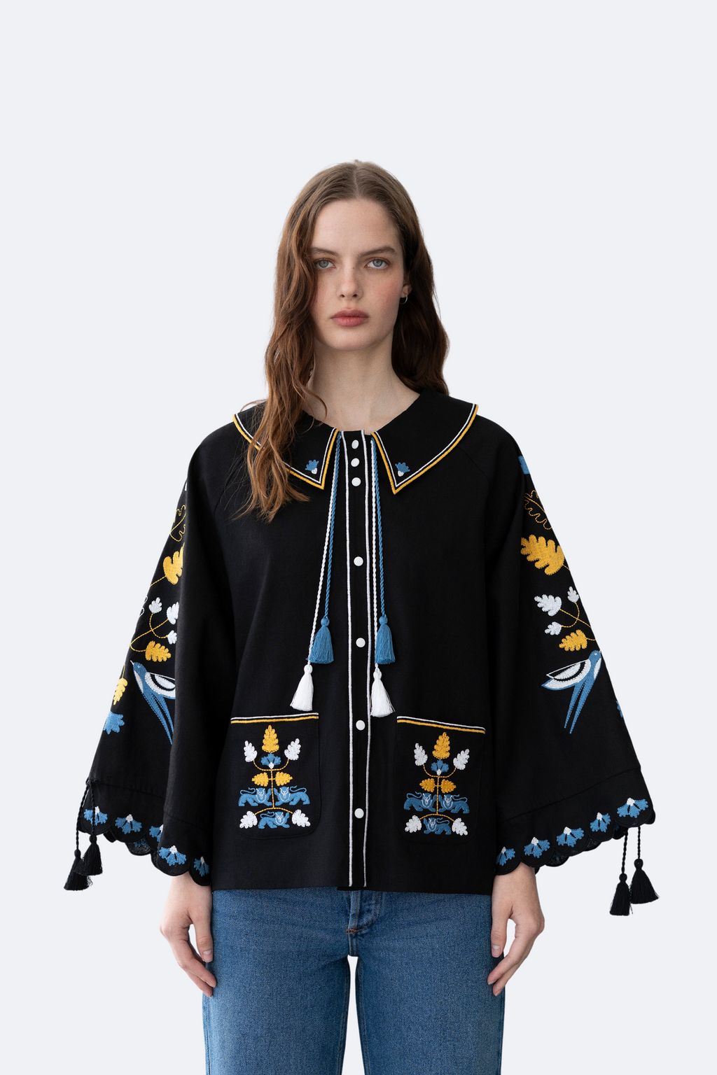 Woman wearing a black embroidered jacket with colorful designs on a white background