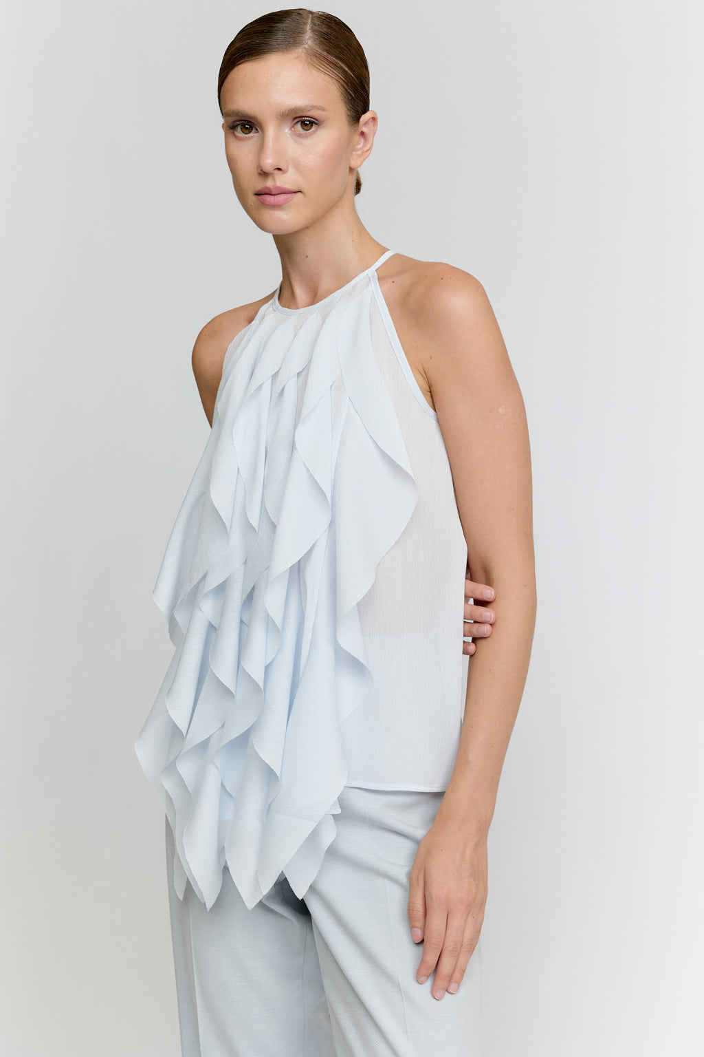 Woman wearing a light blue ruffled top and pants on a white background