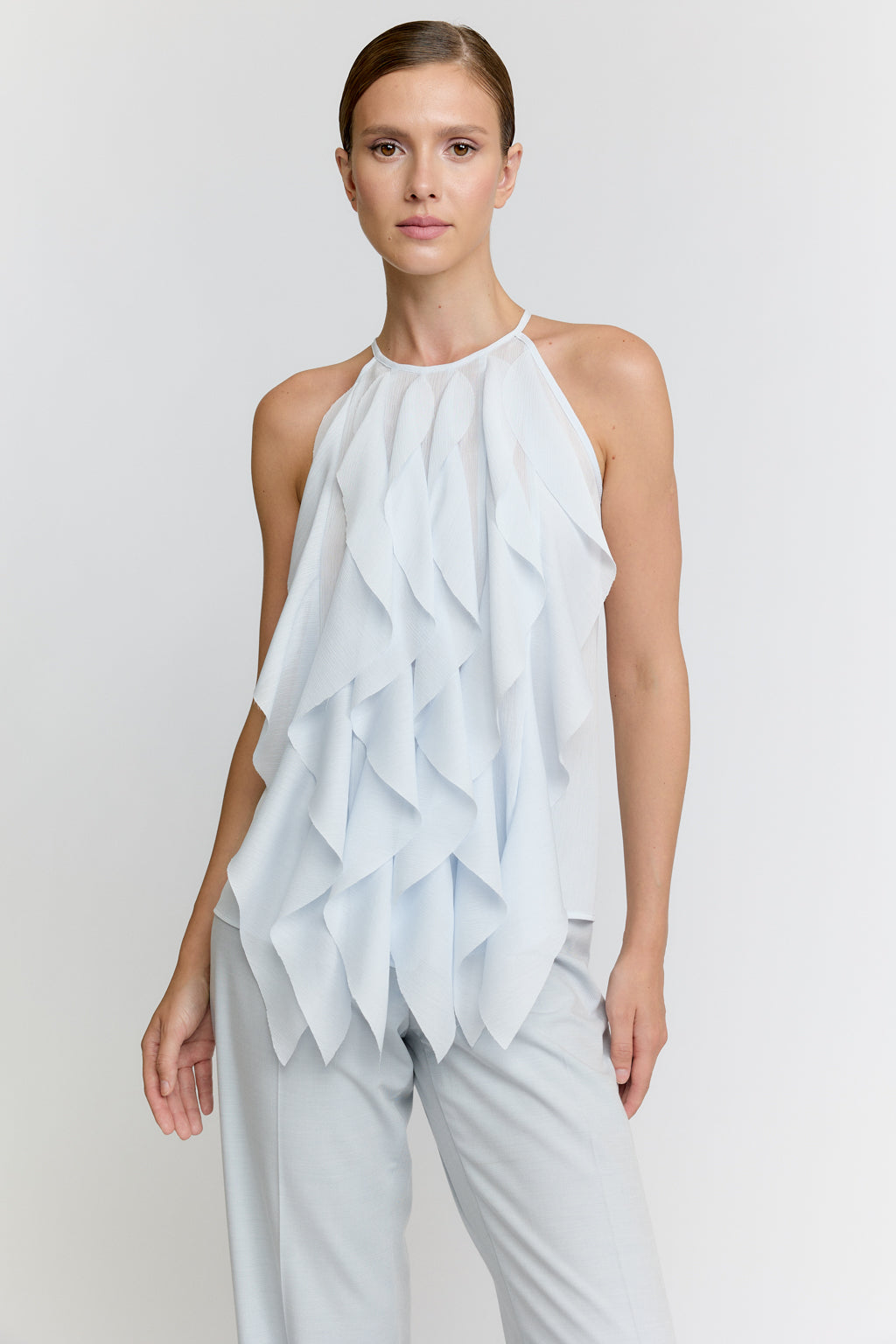 Woman wearing a light blue ruffled top and pants on a plain background