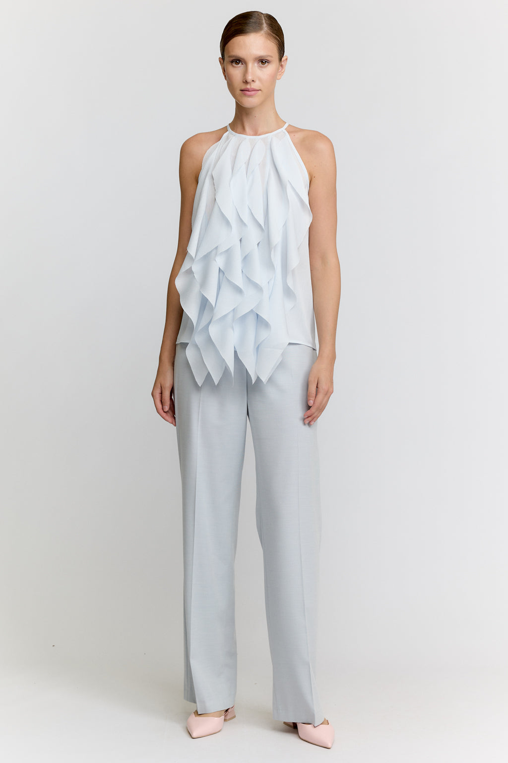 Woman wearing a light blue ruffled top and pants on a white background