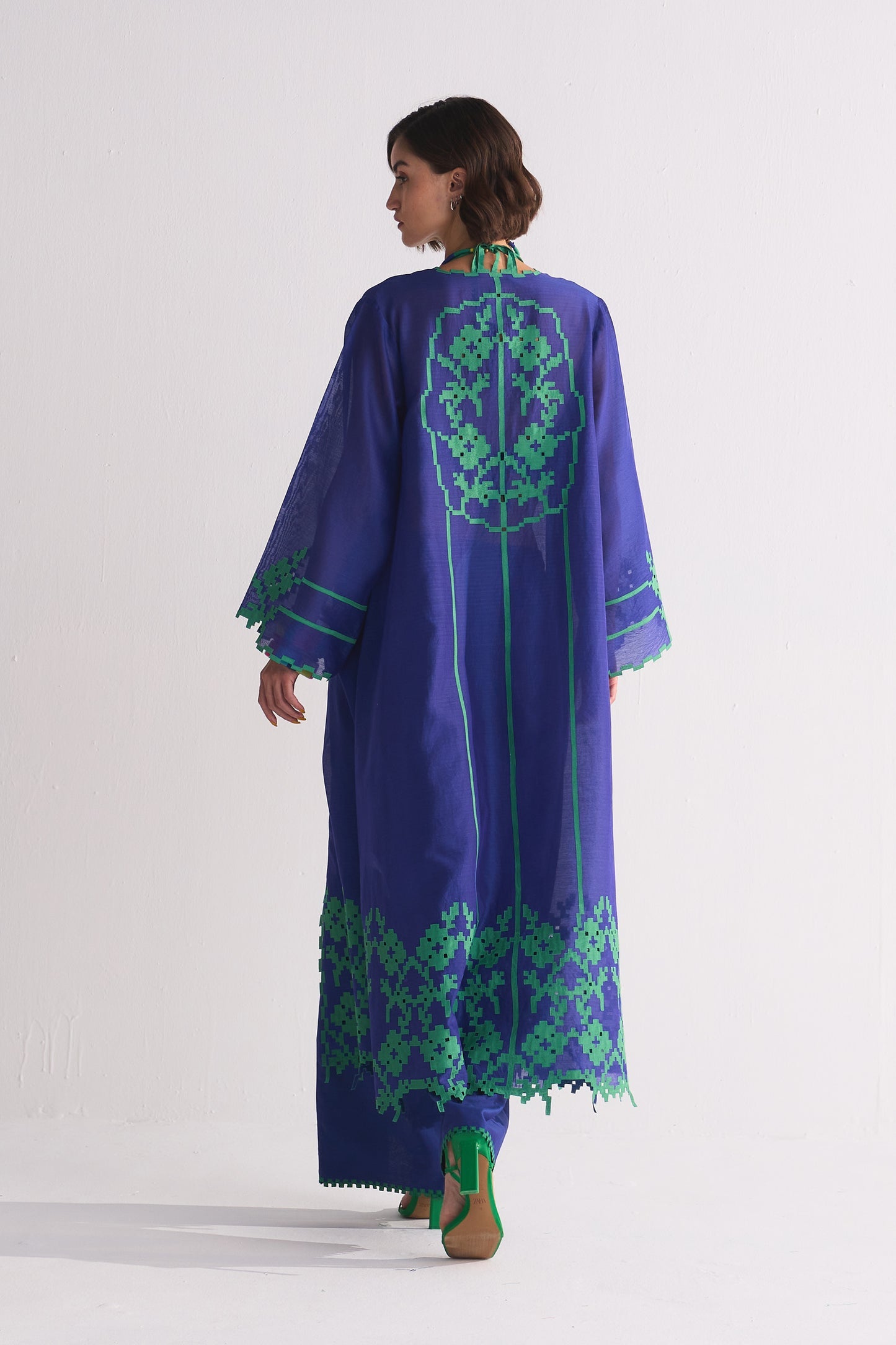 Woman wearing a long blue dress with green embroidery on a white background