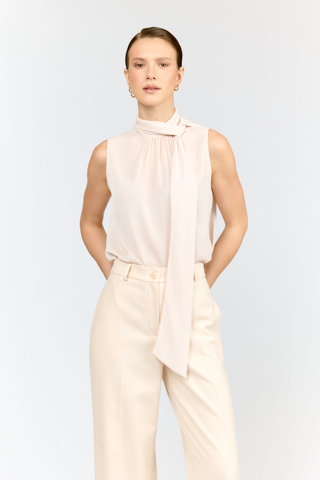 Woman wearing a sleeveless top and pants with a scarf on a white background