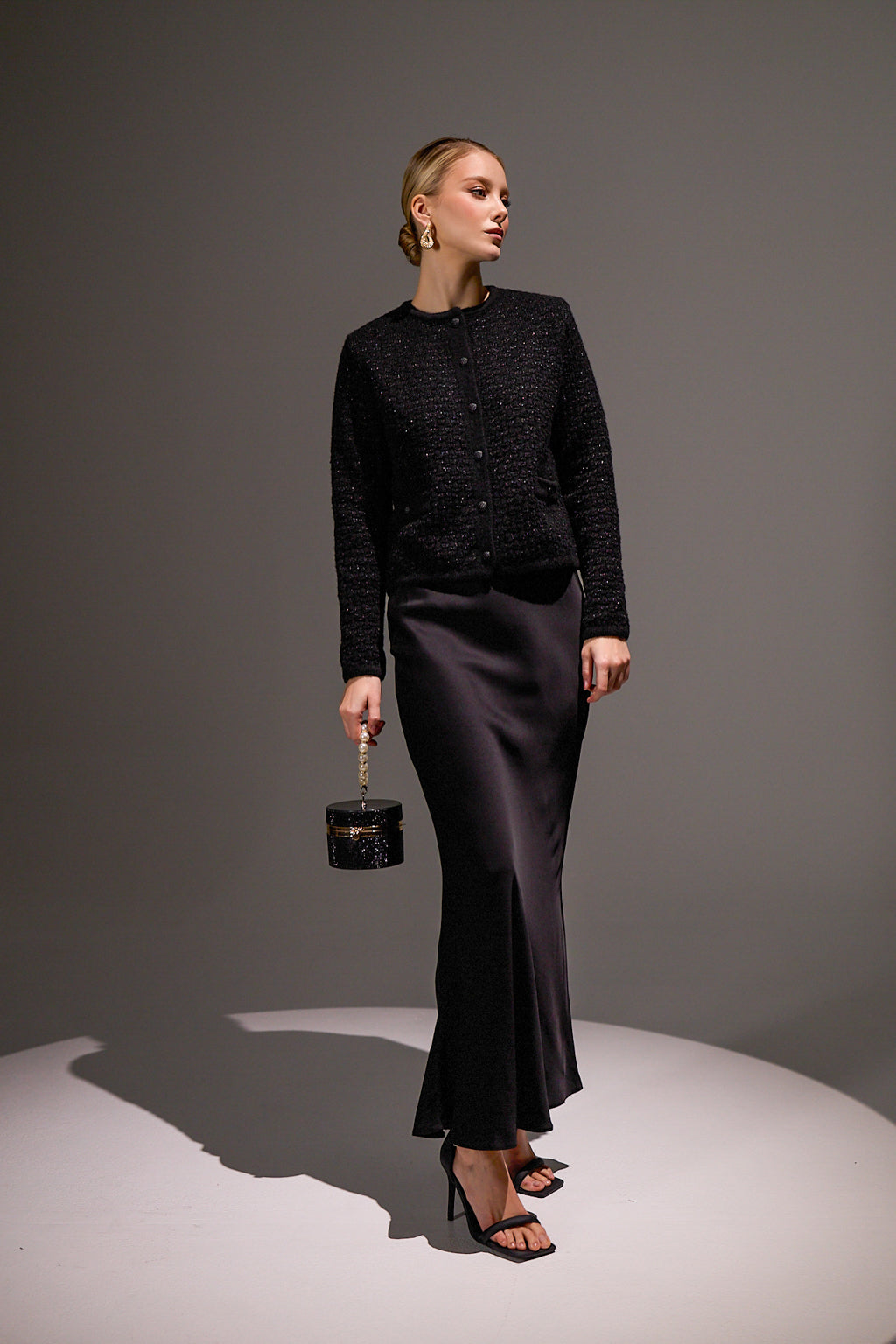 Woman in a black outfit holding a small black handbag against a gray background