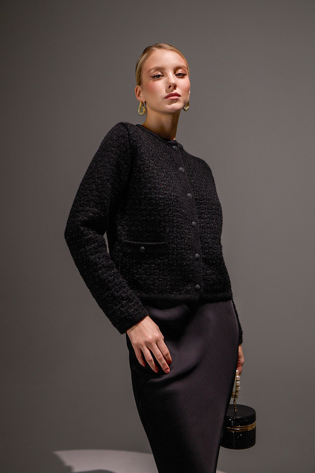 Woman wearing a black textured jacket and skirt with a gray background