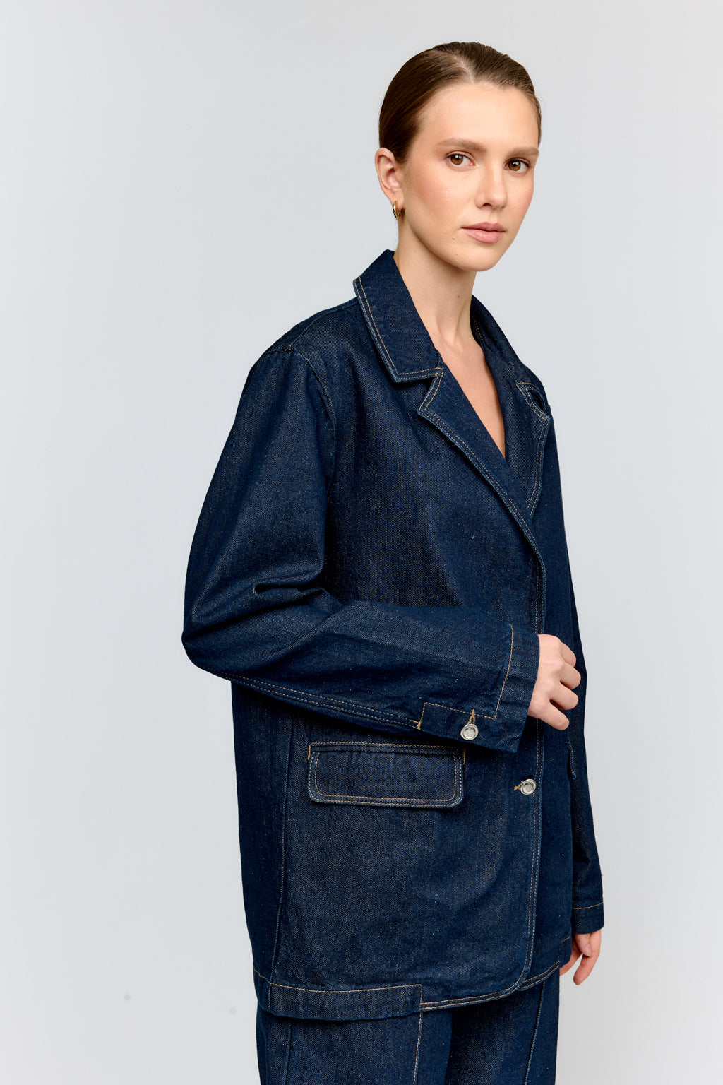 Woman wearing a dark blue denim jacket and pants on a light gray background
