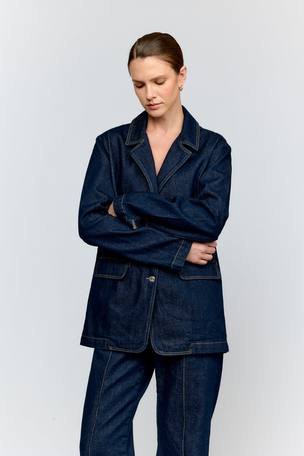 Woman wearing a dark blue denim jacket and pants on a light gray background