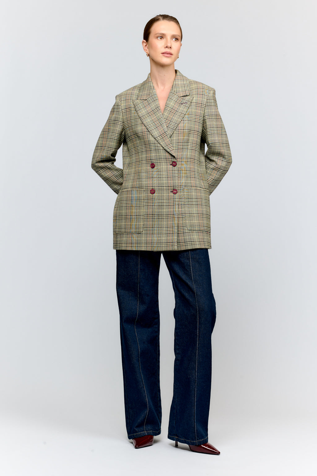 Person wearing a plaid blazer and dark jeans on a white background