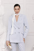 Woman wearing a light blue suit with a white scarf against a white background