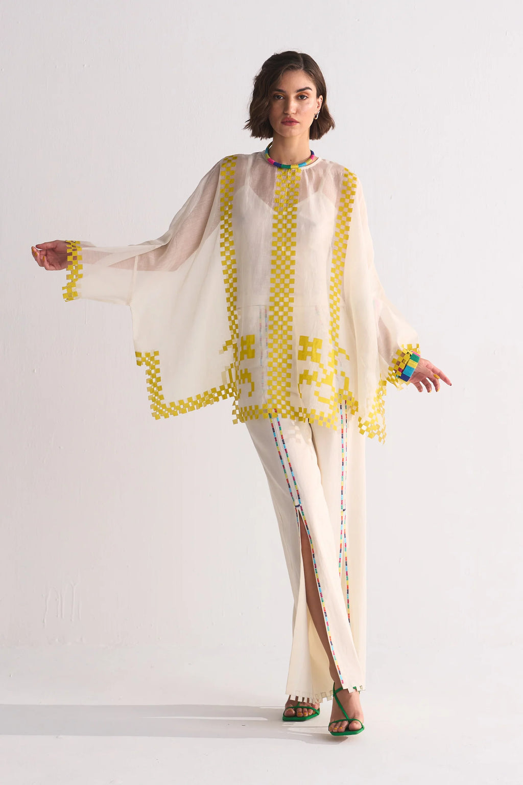 Woman wearing a stylish outfit with a sheer top and pants on a white background