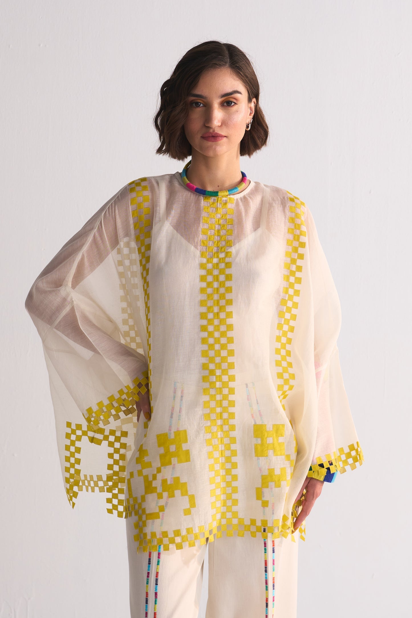 Woman wearing a white outfit with yellow patterns on a plain background