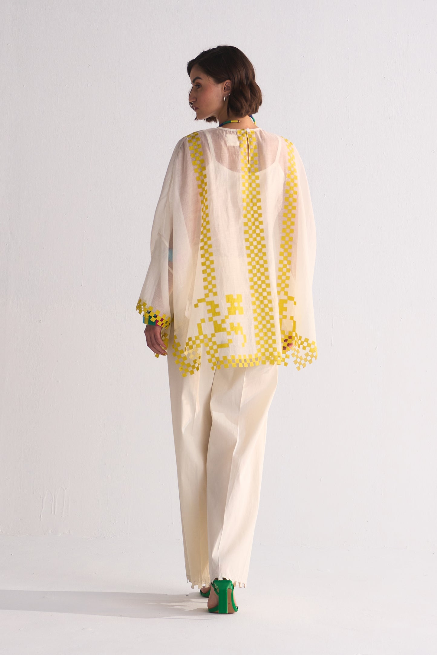Woman wearing a cream outfit with yellow patterns on a white background