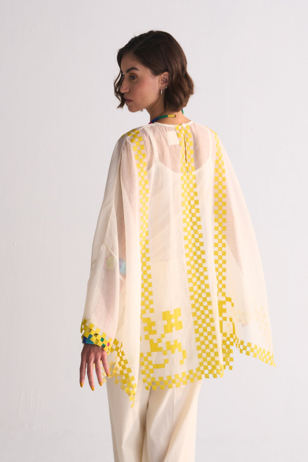 Woman wearing a cream outfit with yellow embroidery on a white background
