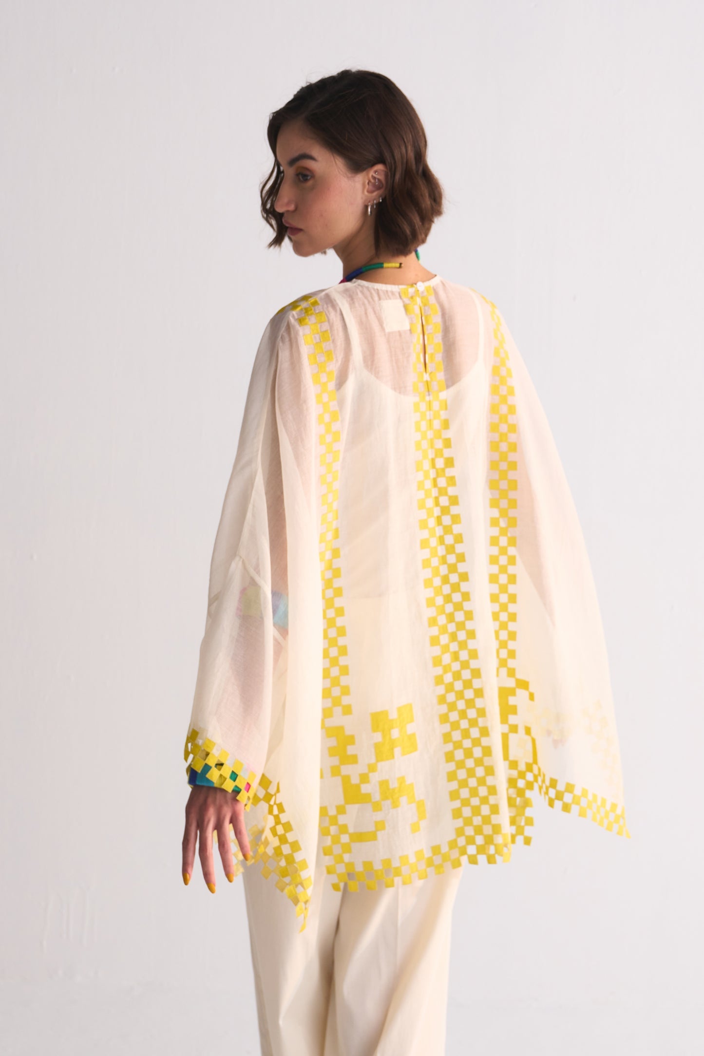Woman wearing a cream outfit with yellow embroidery on a white background
