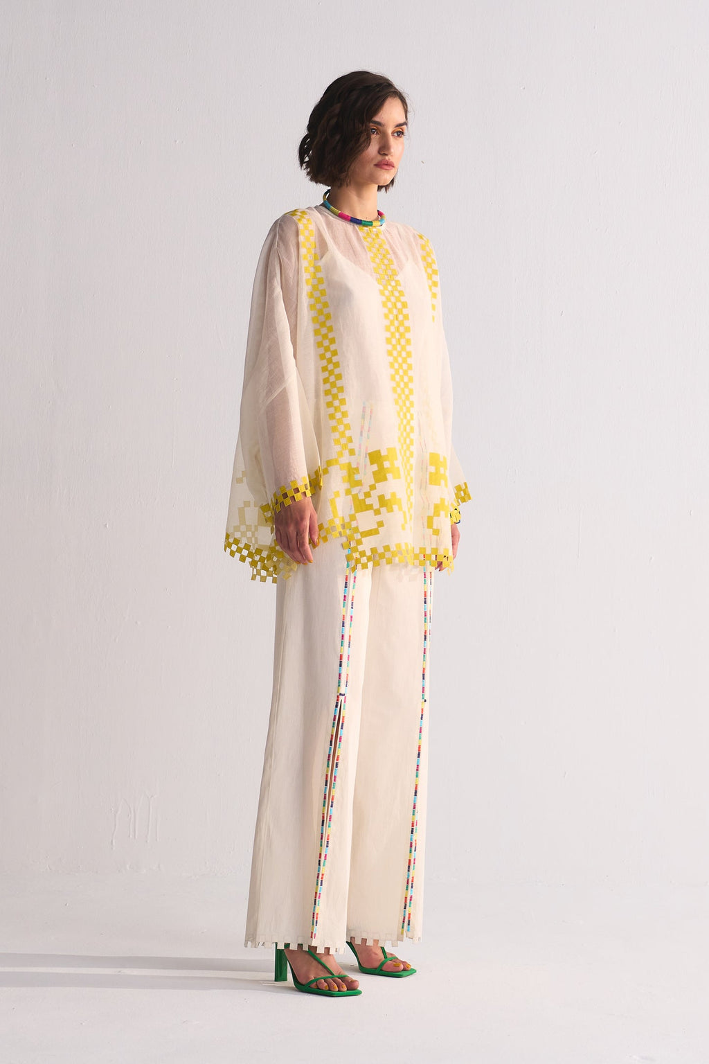 Woman wearing a cream outfit with yellow accents on a white background