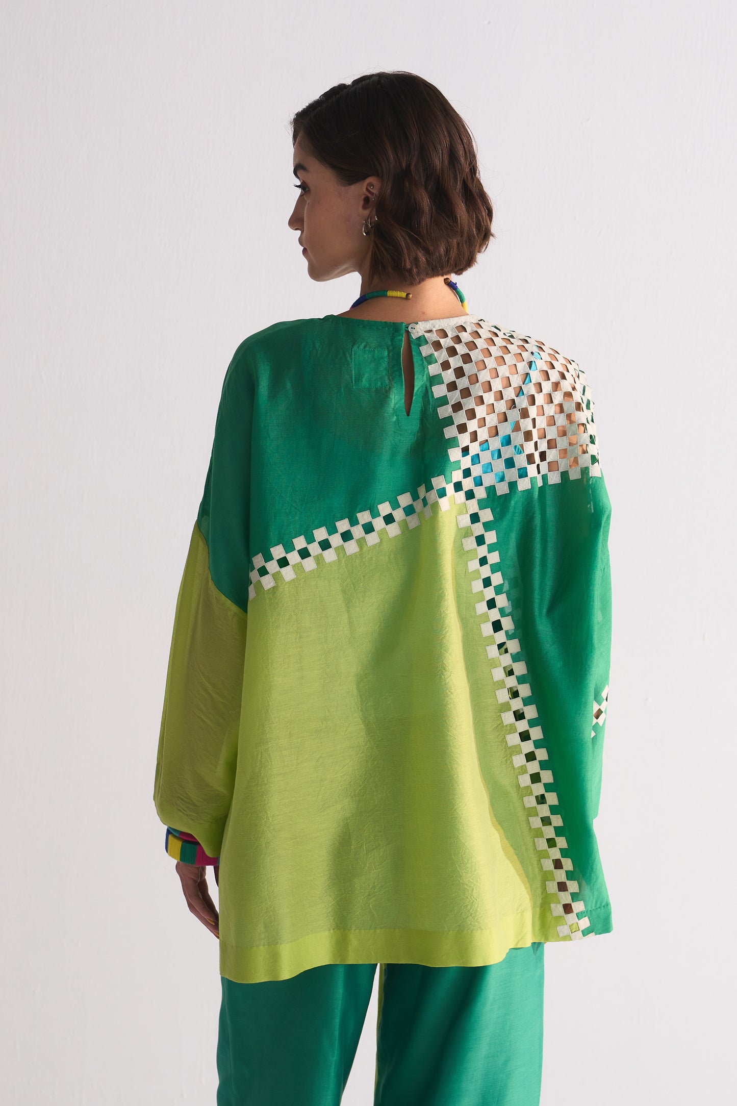 Woman wearing a green and yellow traditional outfit with a white and black patterned design on a white background