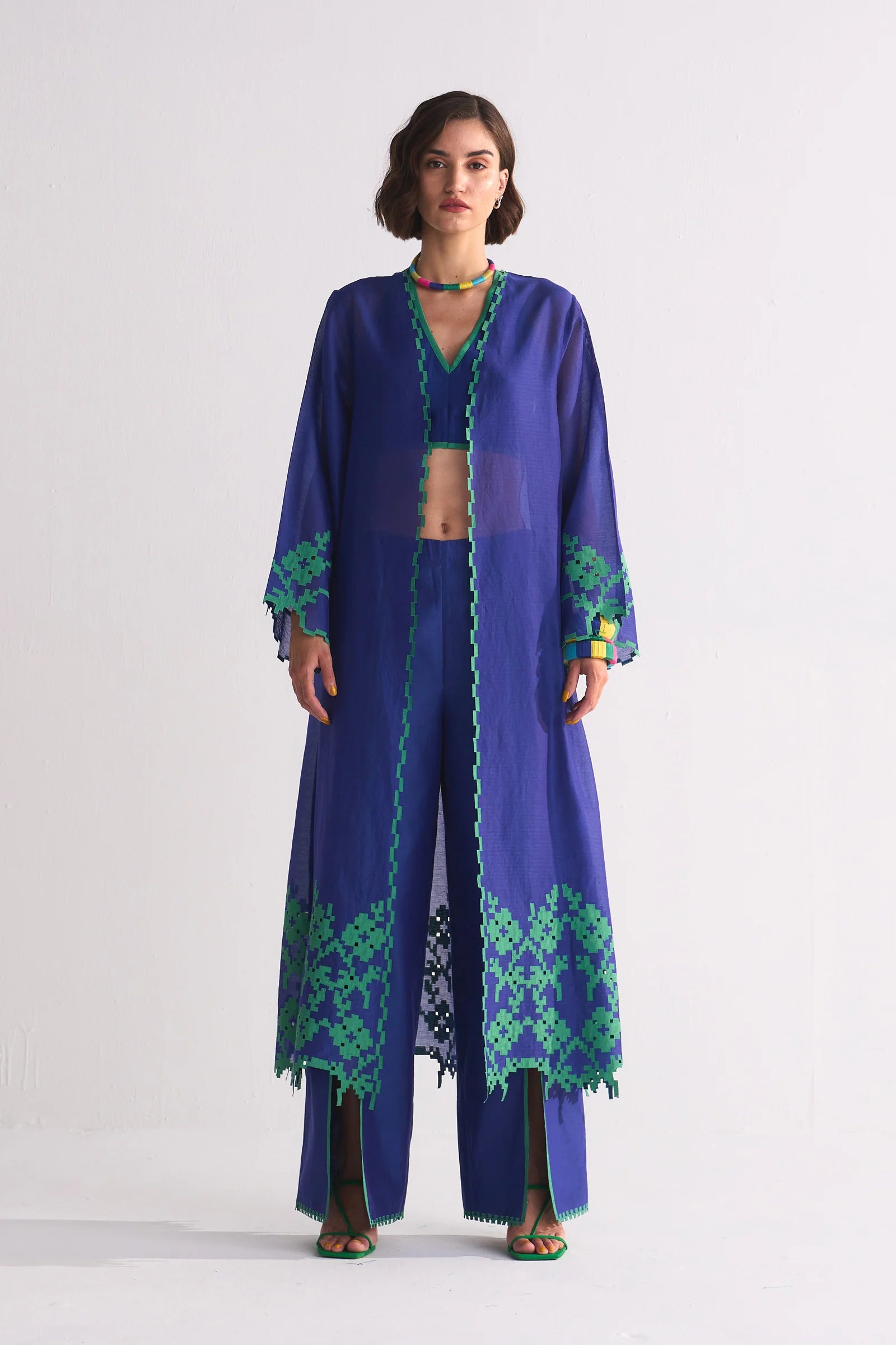 Woman wearing a long blue dress with green patterns on a white background