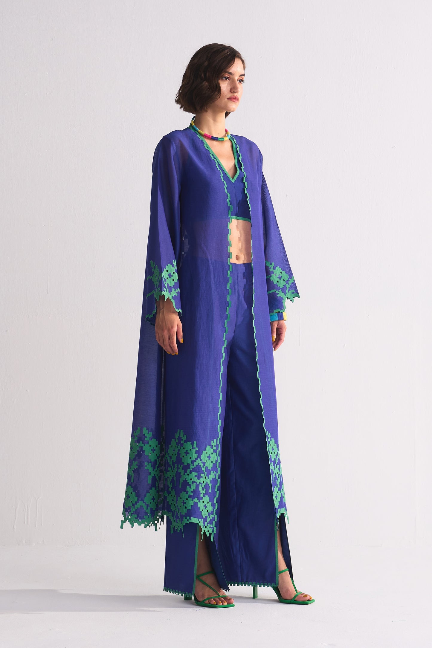 Woman wearing a long blue embroidered robe with green patterns on a white background