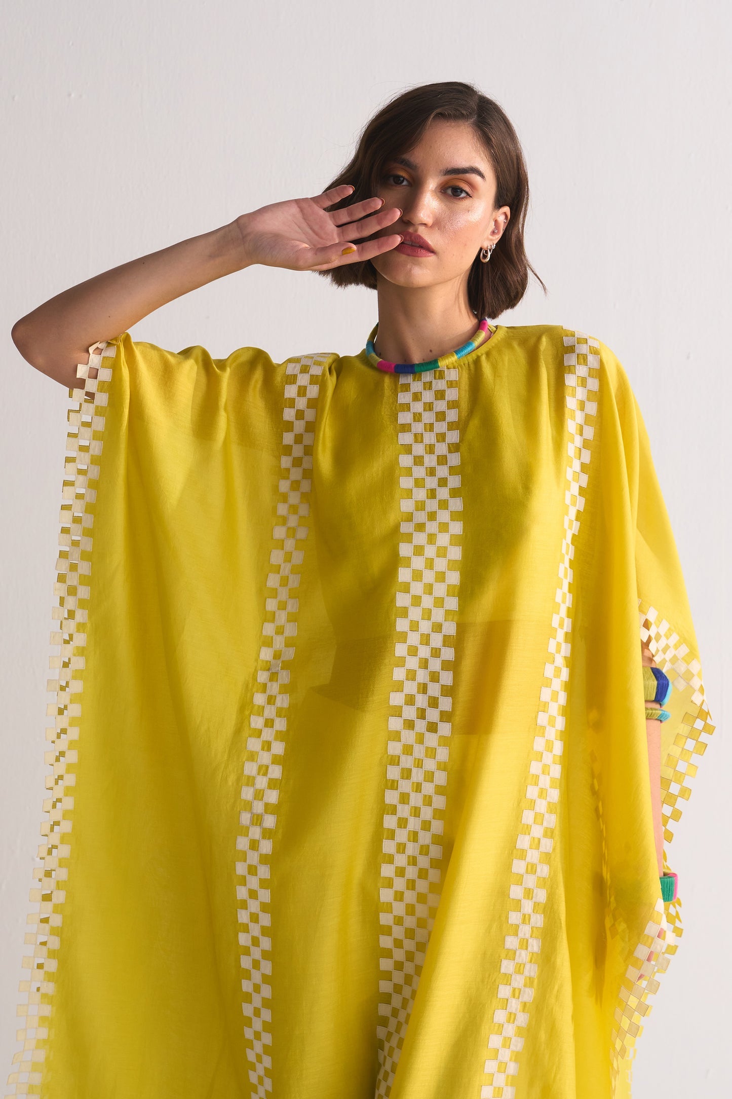 Woman wearing a yellow traditional outfit with a white checkered border on a plain background