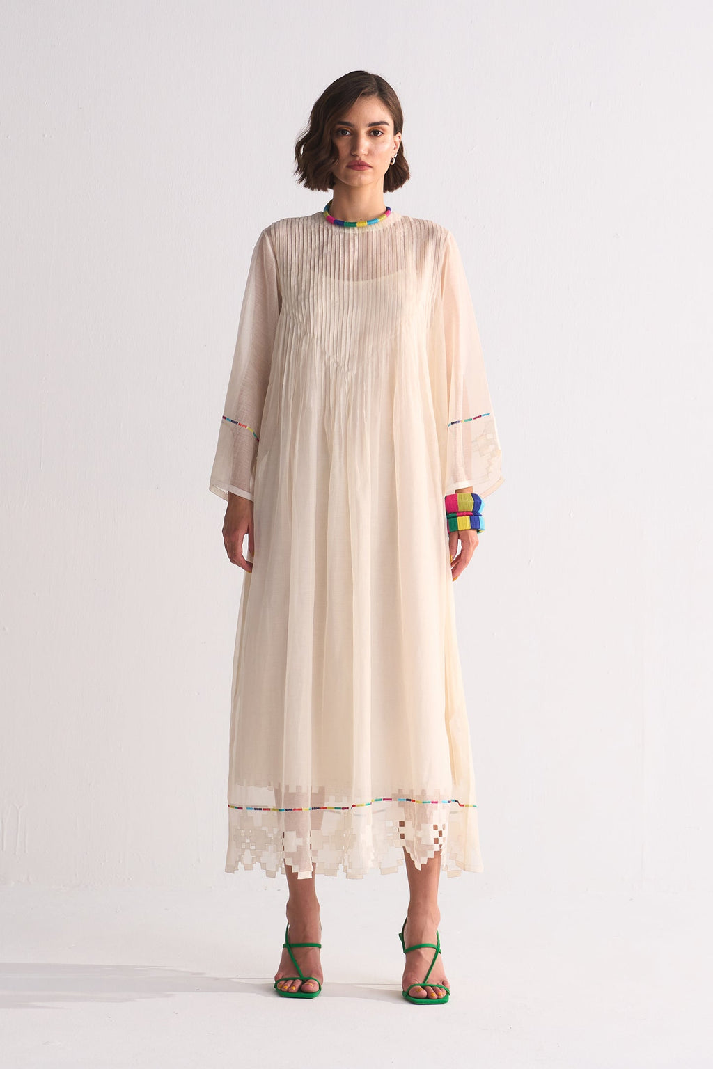 Woman wearing a long, light-colored dress with sheer sleeves on a white background