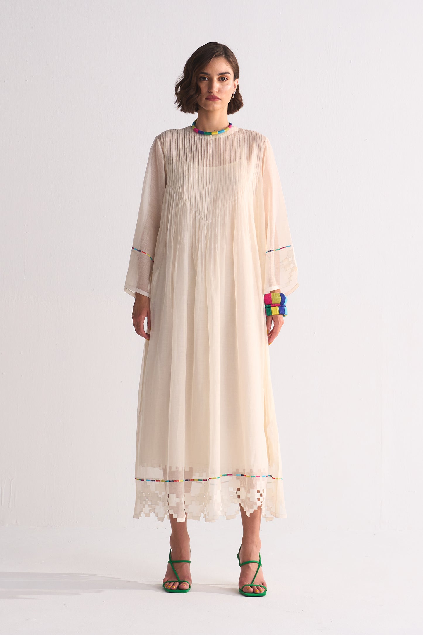 Woman wearing a long, light-colored dress with sheer sleeves on a white background