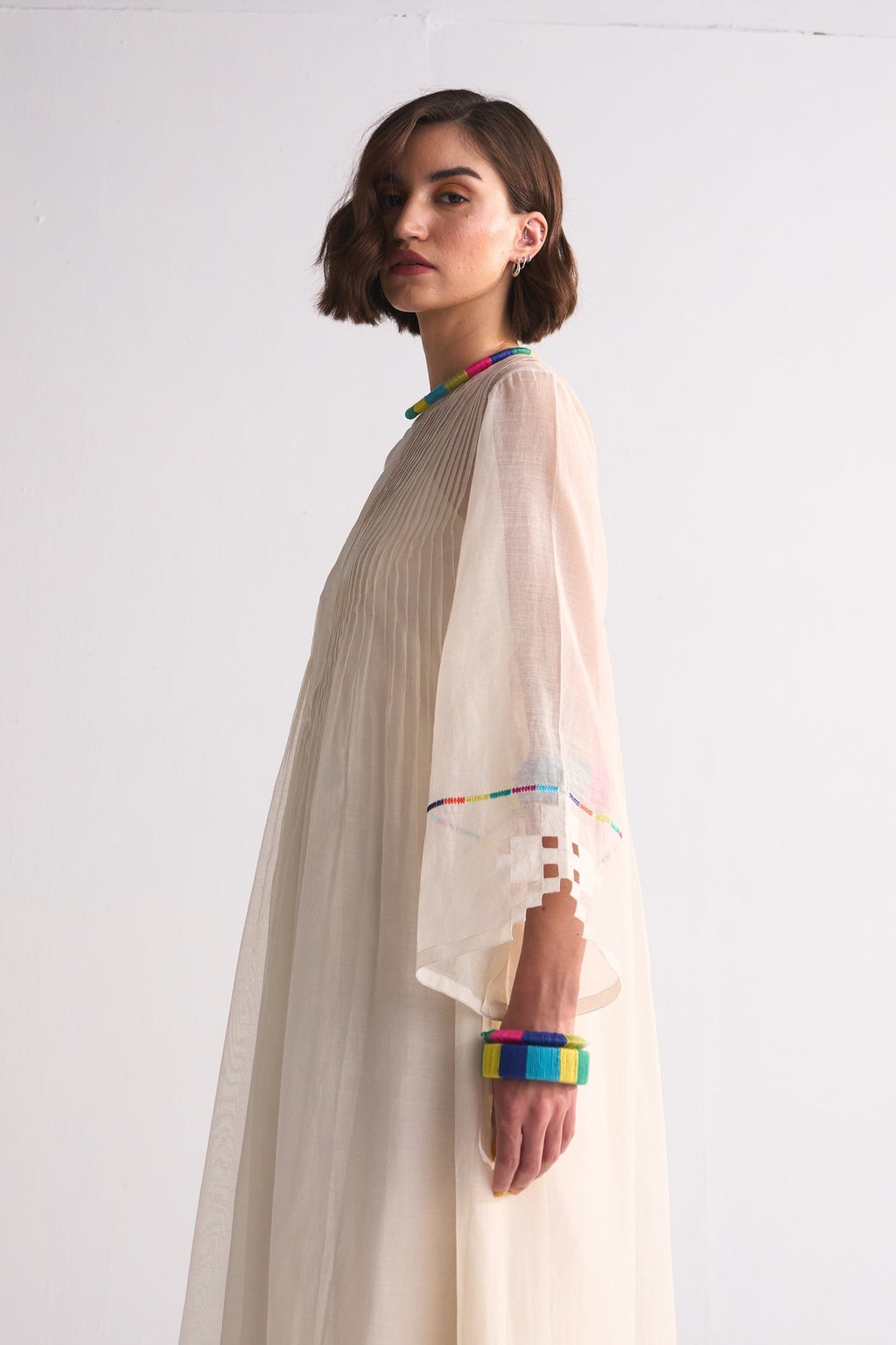 Woman wearing a long beige dress with colorful accents on a white background