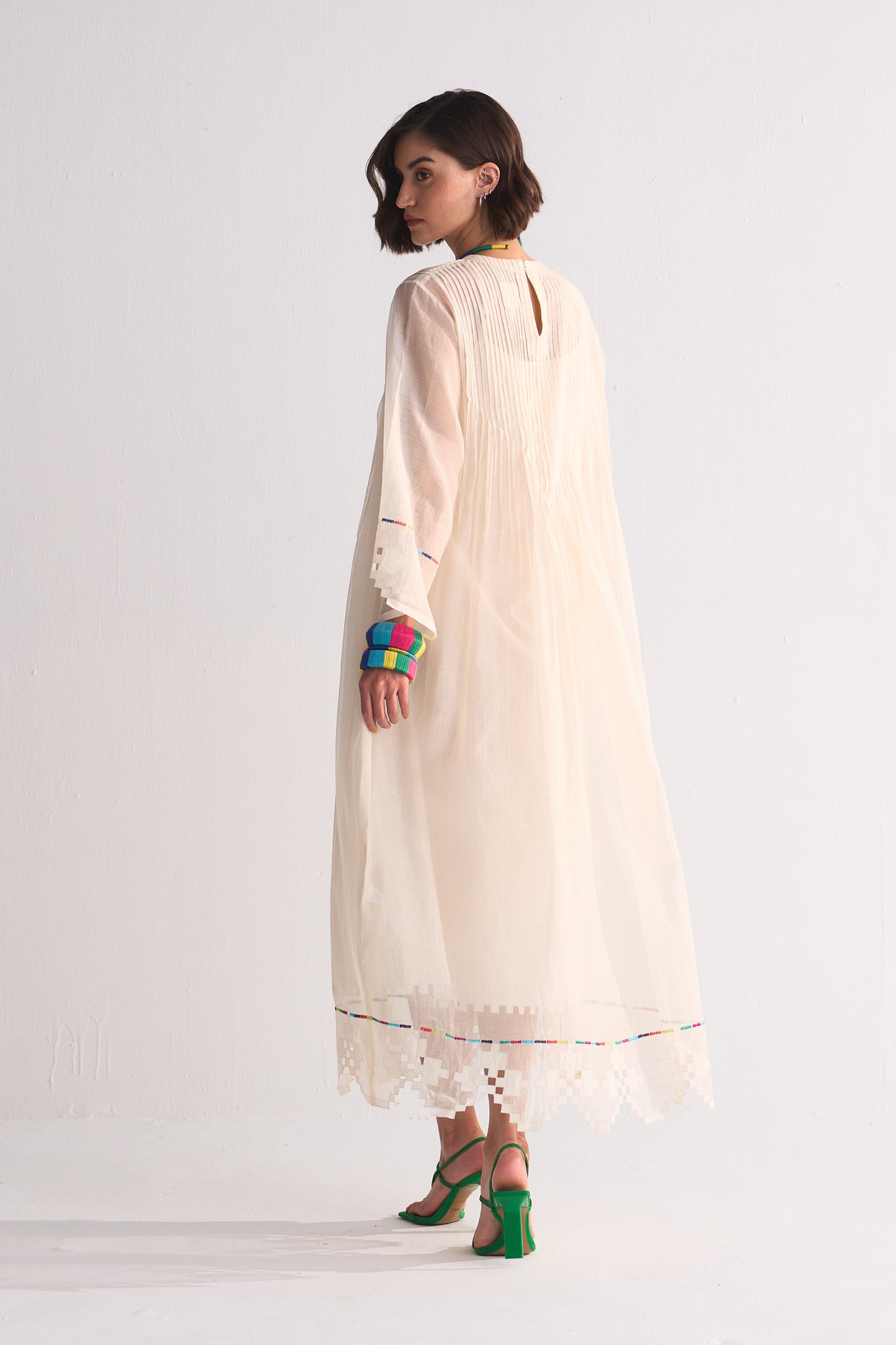 Woman wearing a long beige dress with colorful arm bands on a white background