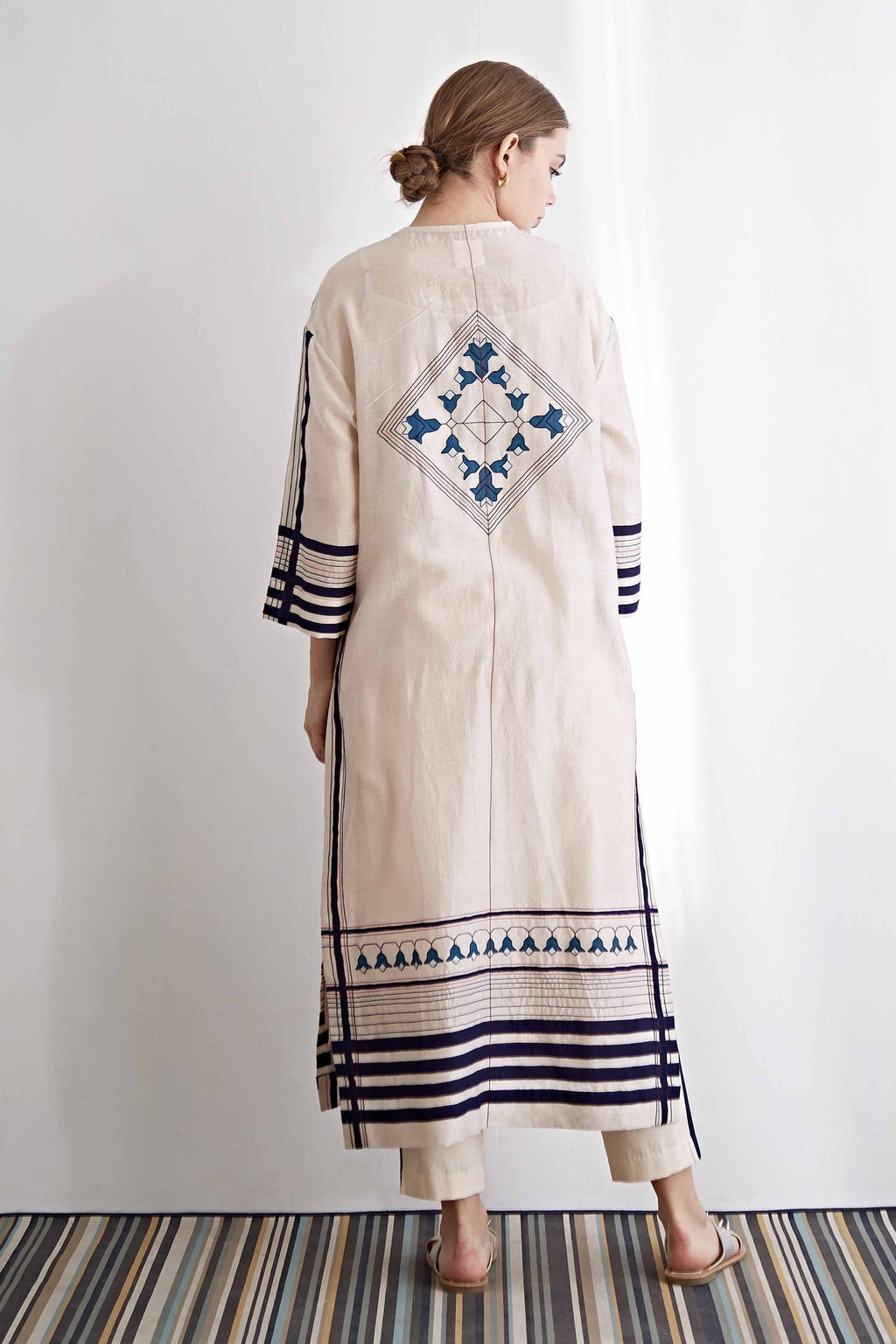 Woman wearing a long, embroidered dress with geometric patterns on a white background