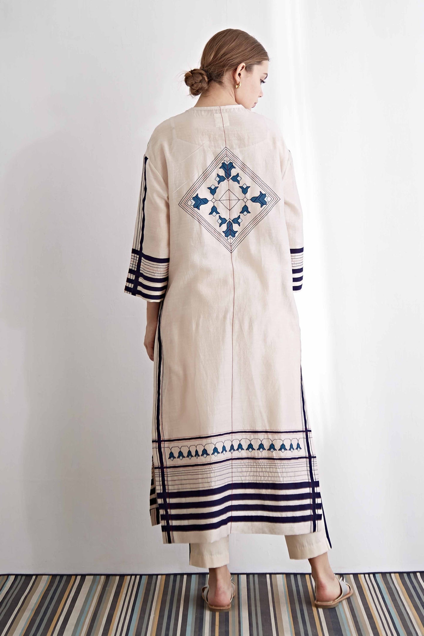 Woman wearing a long, embroidered dress with geometric patterns on a white background