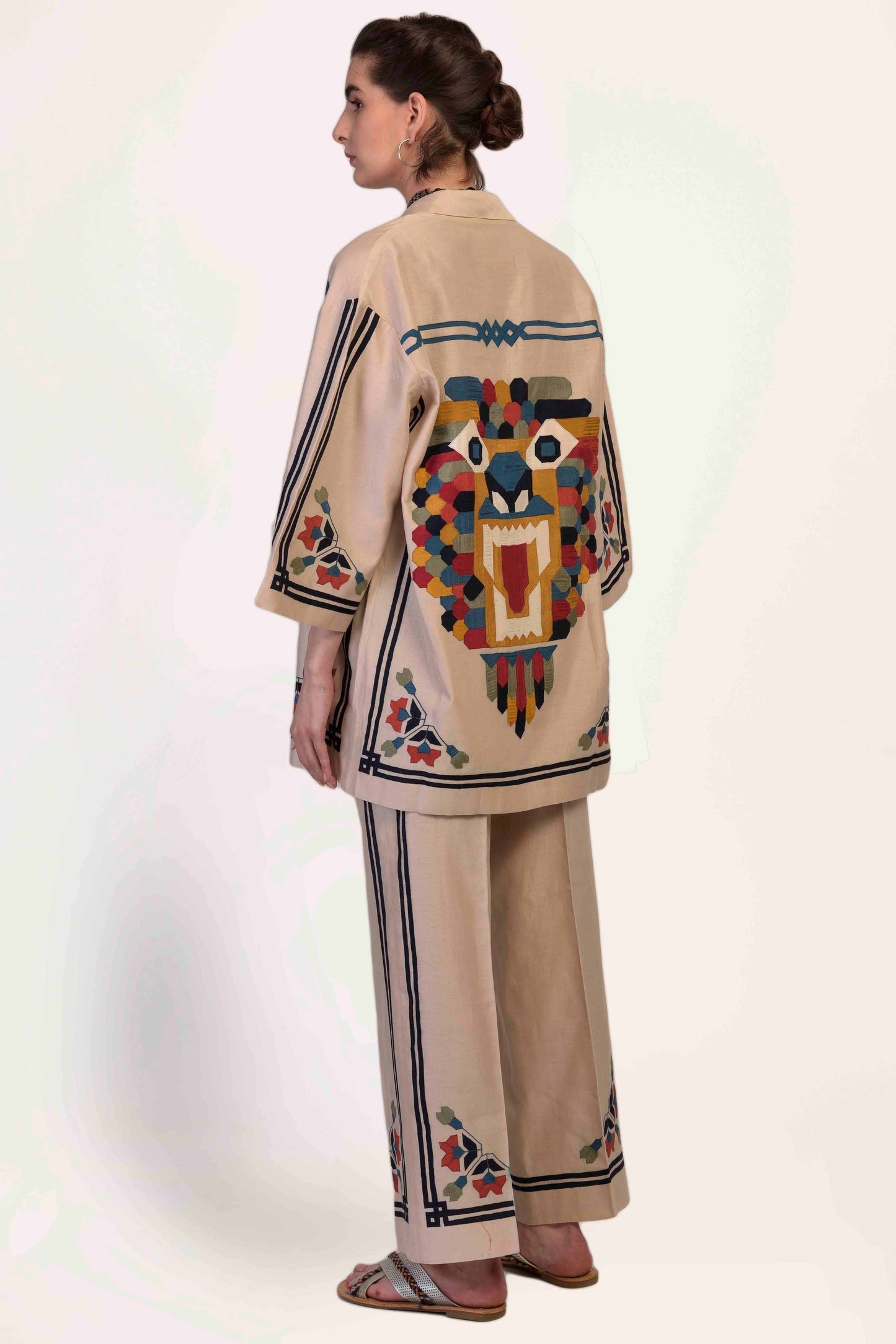 Woman wearing a beige outfit with colorful embroidery on a white background