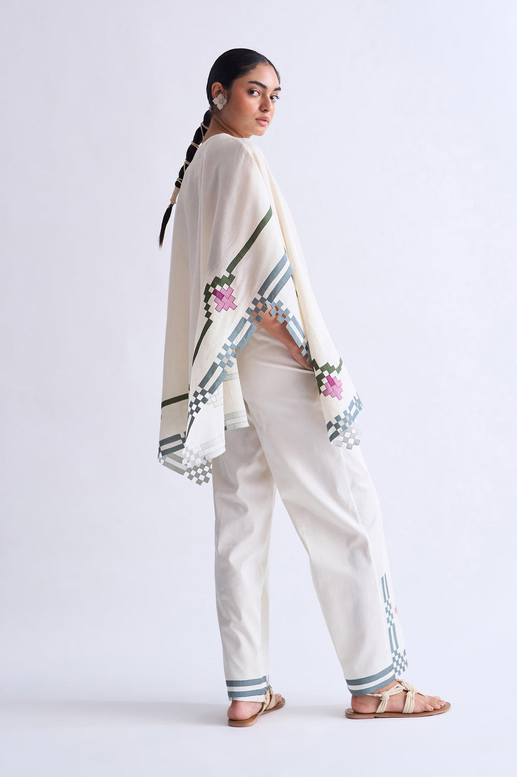 Woman wearing a traditional outfit with a white shawl and embroidered pants on a light gray background