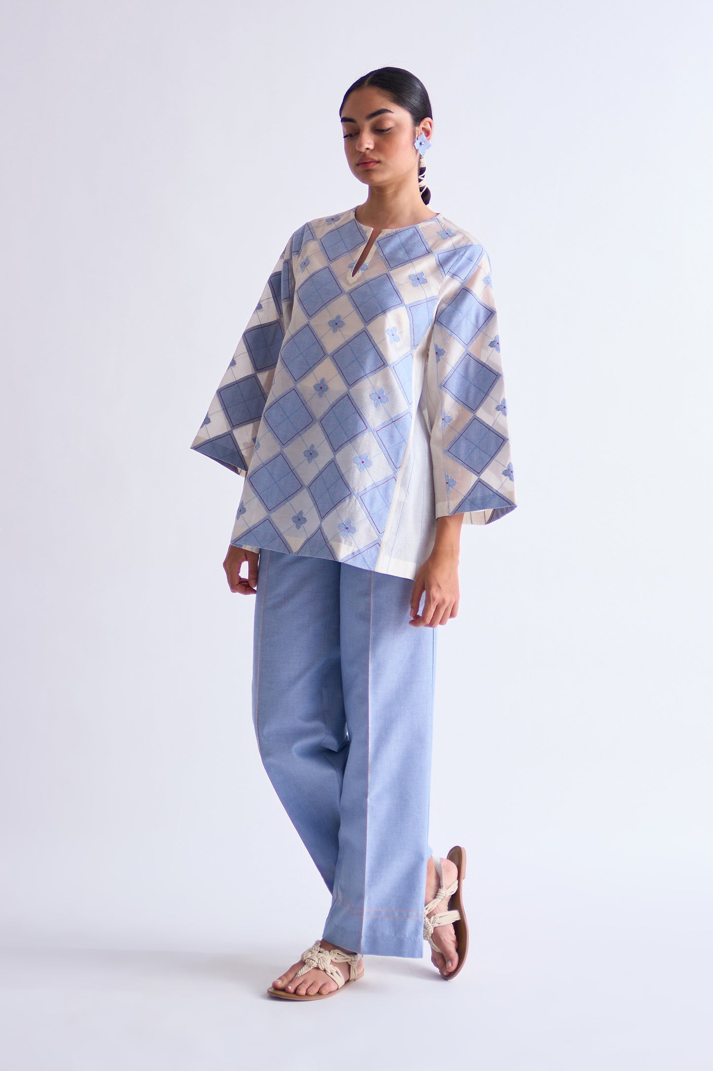 Woman wearing a blue and white checkered poncho with light blue pants on a white background