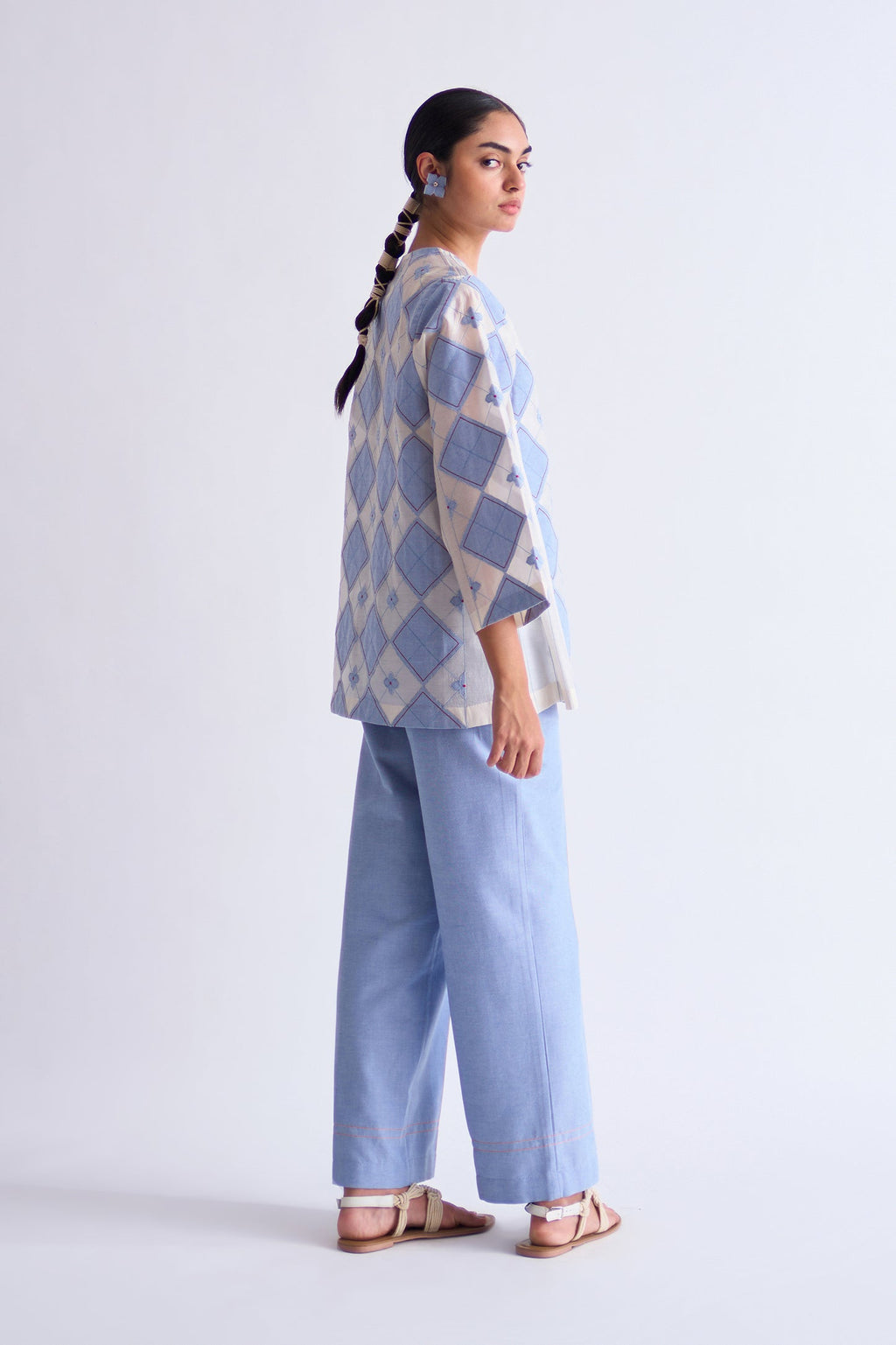 Woman wearing a patterned top and light blue pants on a white background
