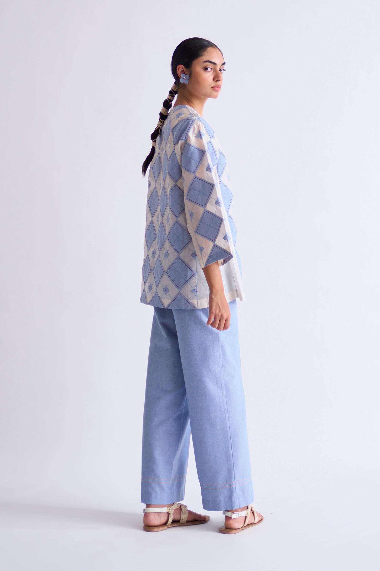 Woman wearing a patterned top and light blue pants on a white background