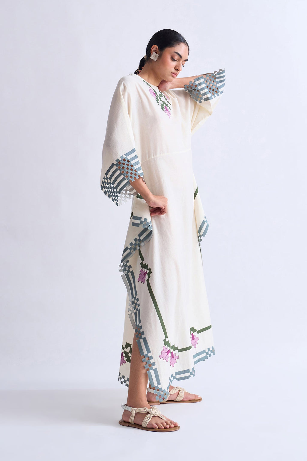 Woman wearing a long, light-colored dress with geometric patterns on a white background