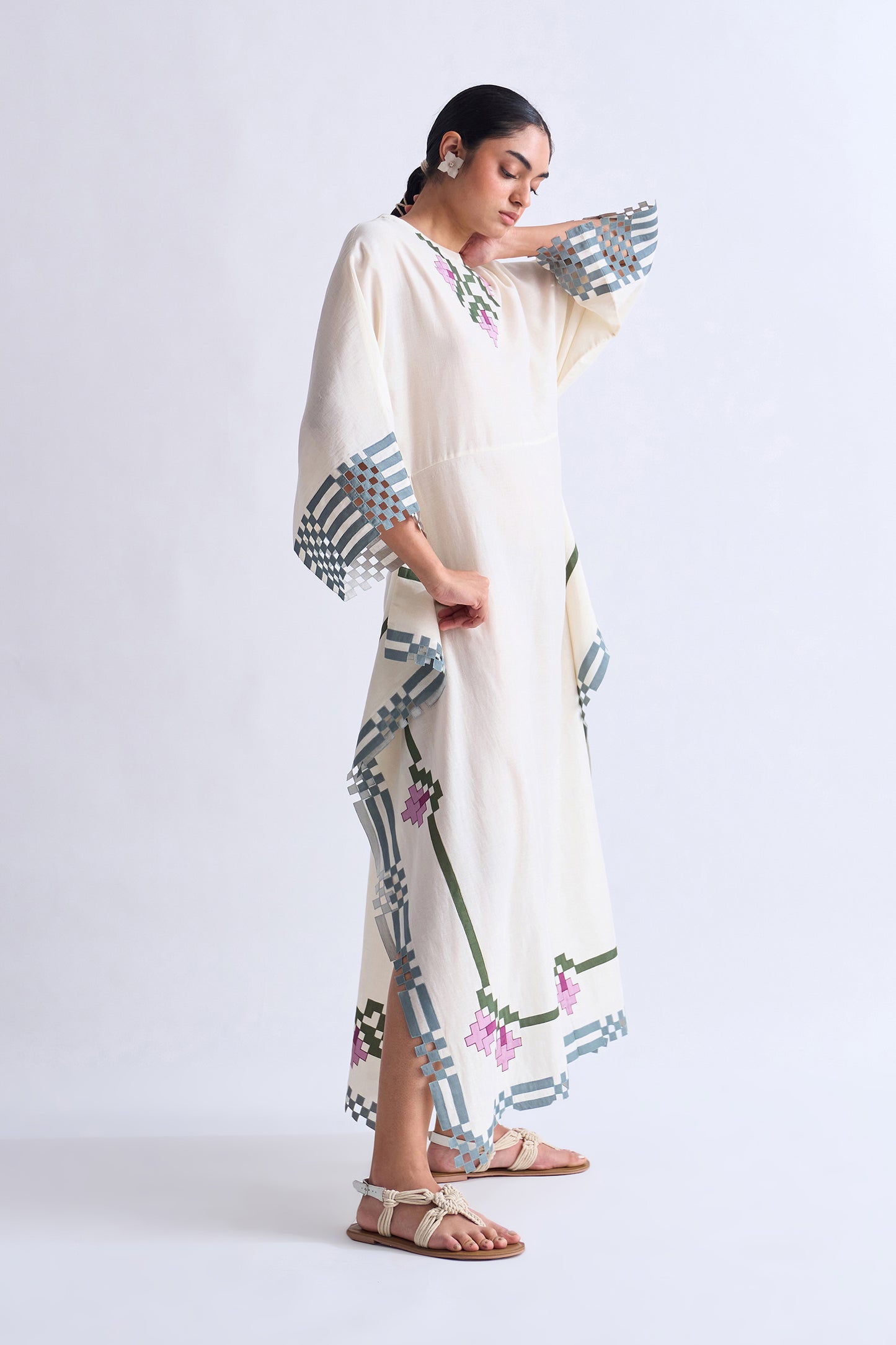 Woman wearing a long, light-colored dress with geometric patterns on a white background