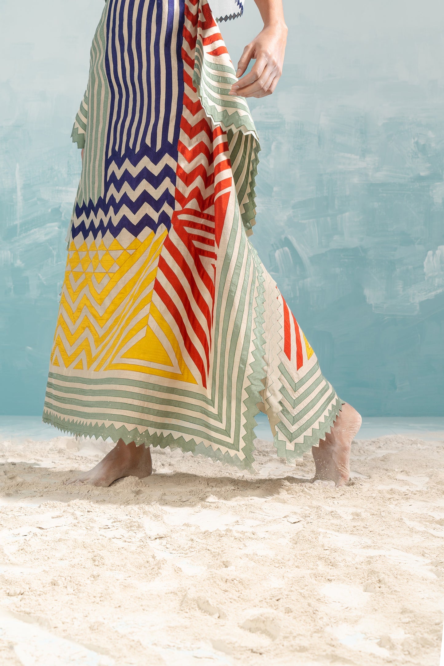 Person wearing a colorful striped dress on a beach with a blue sky background