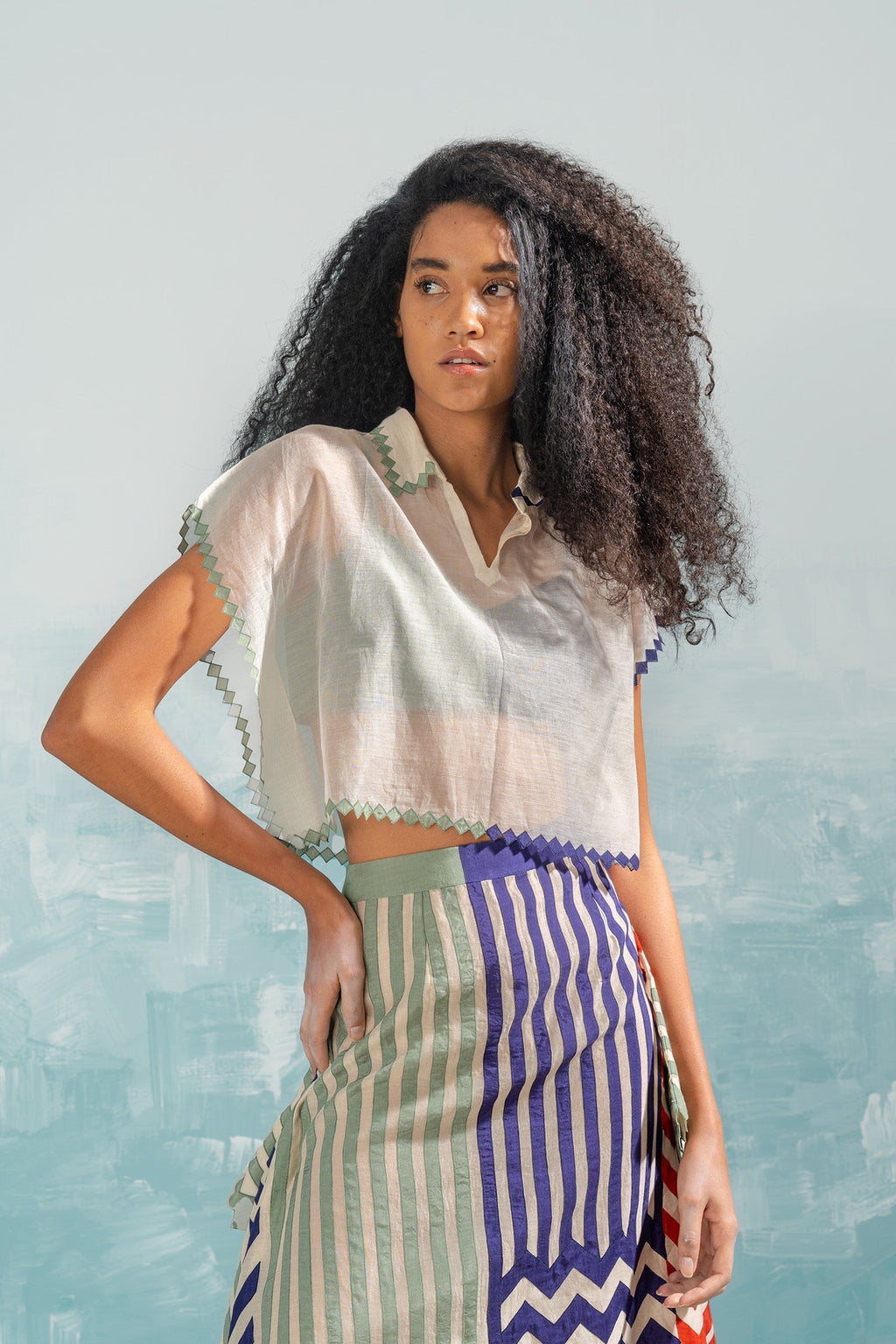 Woman wearing a white blouse with lace details and a colorful skirt against a light blue background